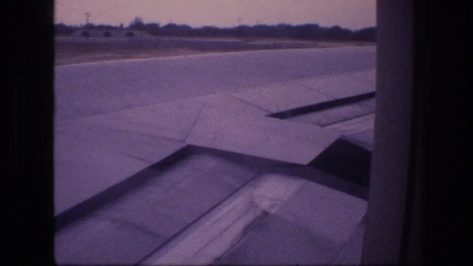 Final frame shows the wing, flap panels, runway, and low horizon through the passenger window, consistent with a short 1977 8mm Honolulu air-travel shot.