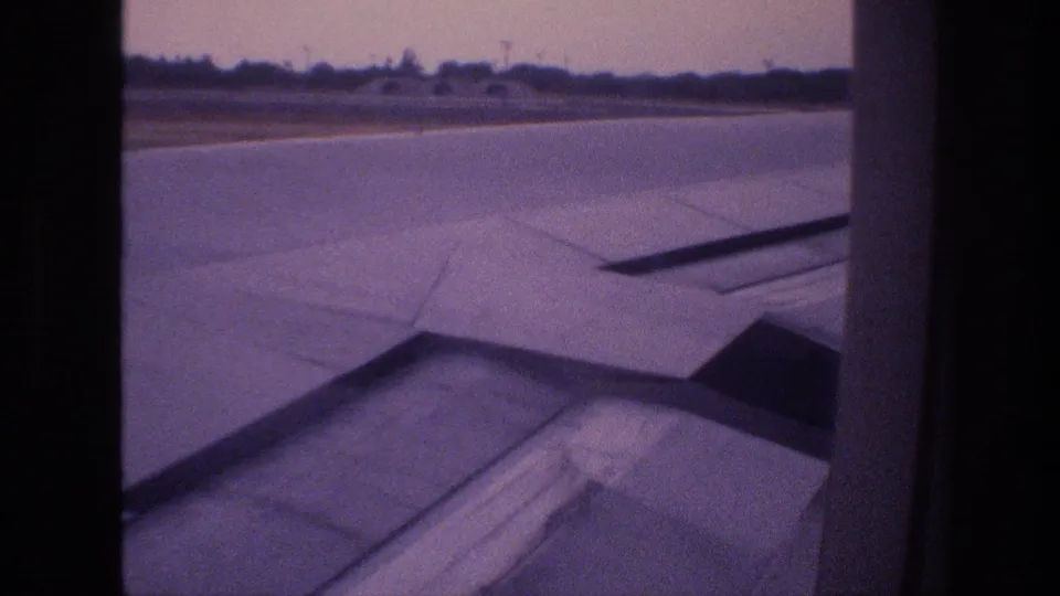1977 Honolulu, Oahu frame with the aircraft wing filling the lower view as the runway and low horizon pass outside the cabin window.