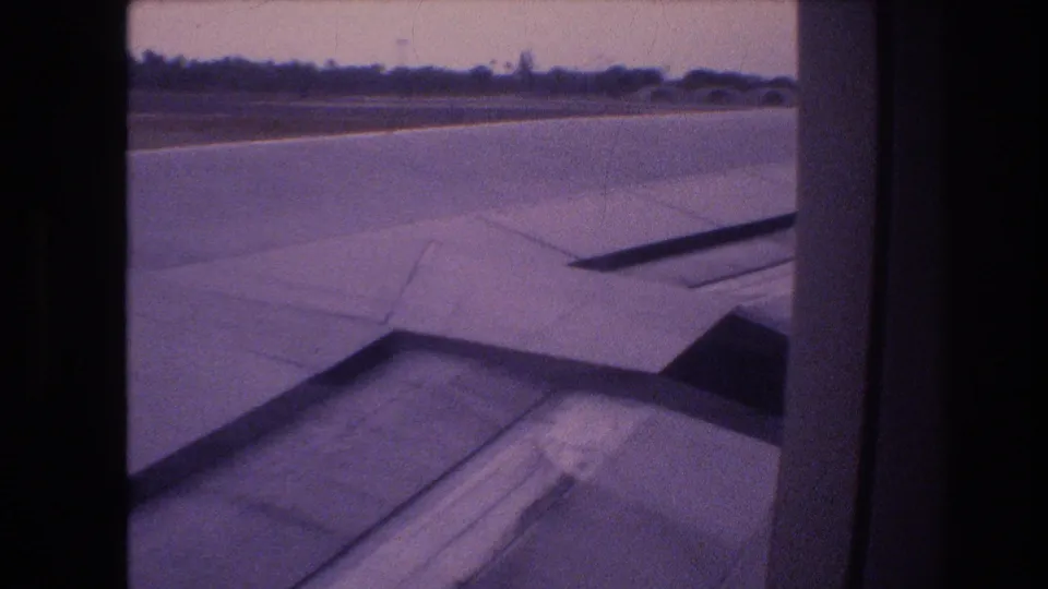 1977 Honolulu, Oahu takeoff frame showing the wing and flap area through the passenger window with runway pavement and a low horizon outside.