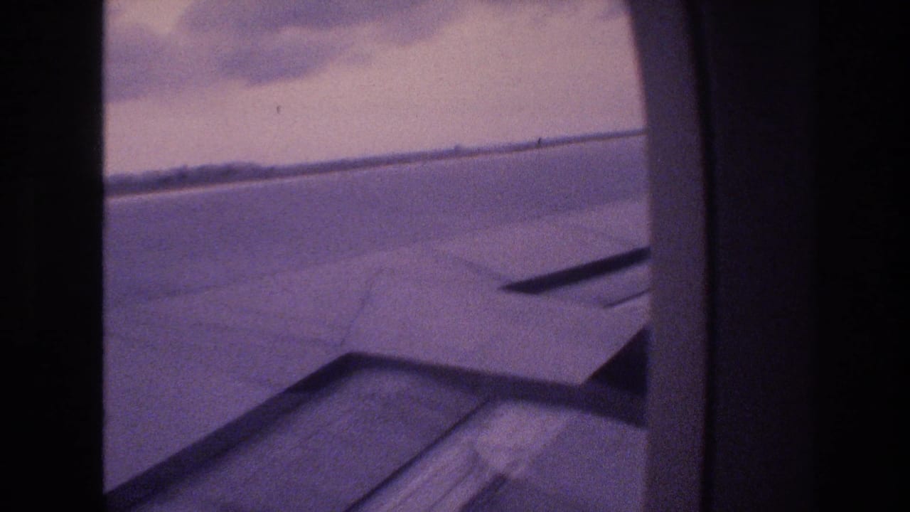 Airplane wing and horizon framed by a rounded aircraft window.