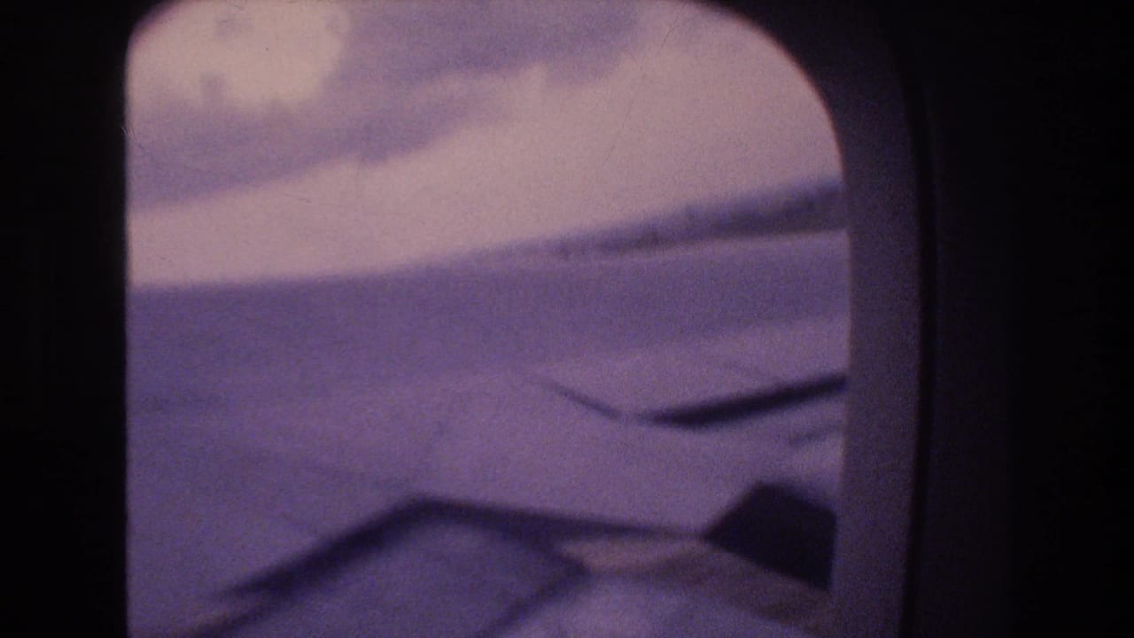Soft 8mm frame of an aircraft wing and cloud bank through a rounded passenger window, consistent with the Honolulu landing metadata.