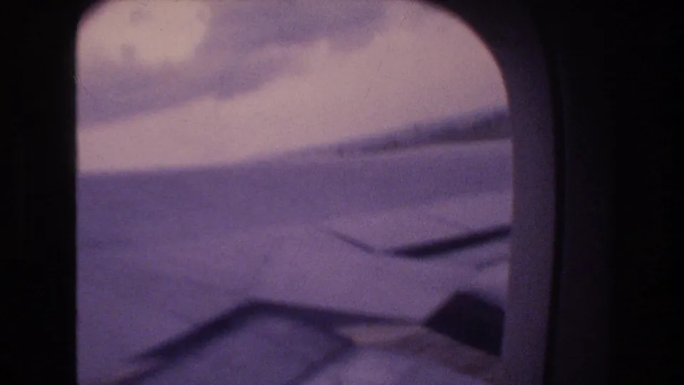 Soft 8mm frame of an aircraft wing and cloud bank through a rounded passenger window, consistent with the Honolulu landing metadata.
