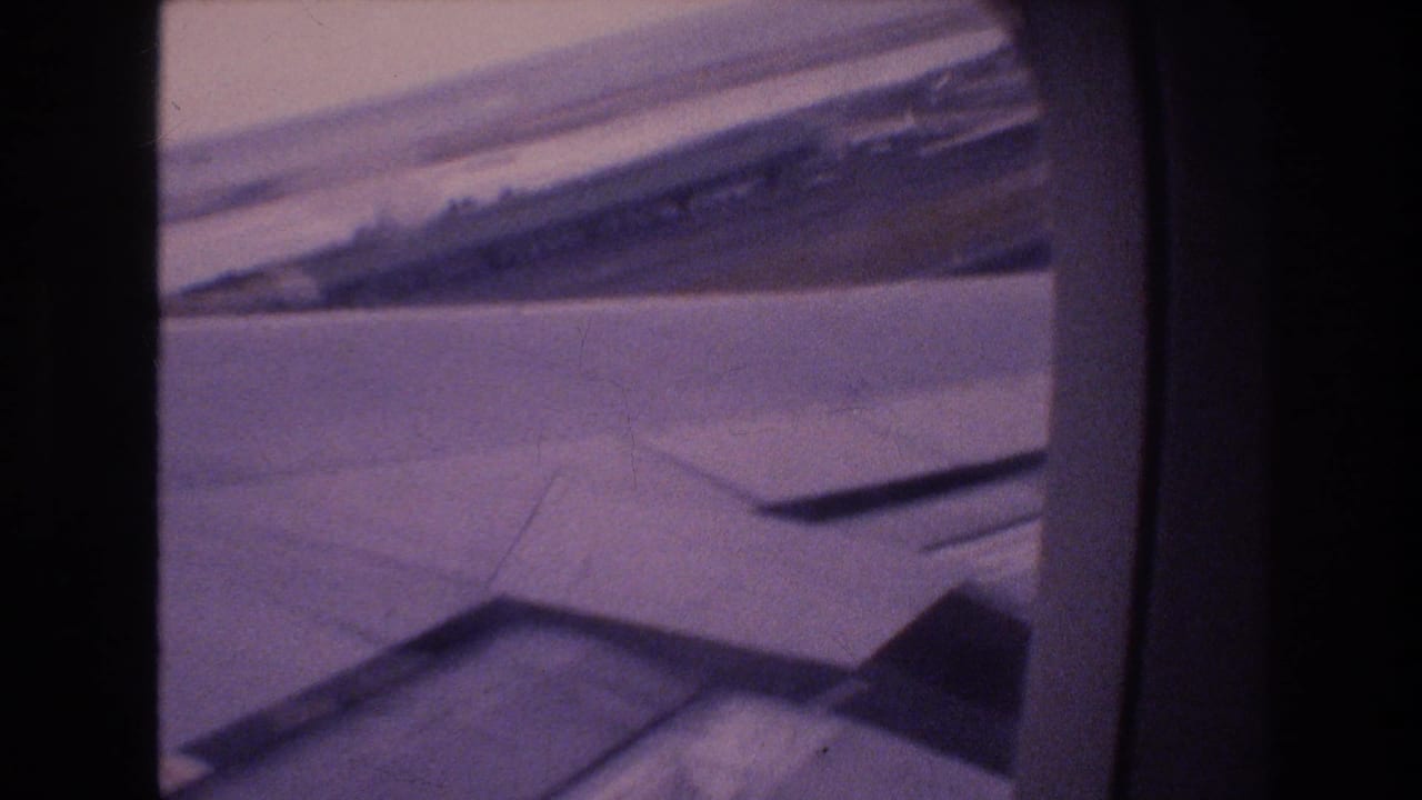 Airplane wing and runway landscape viewed through a rounded passenger window.