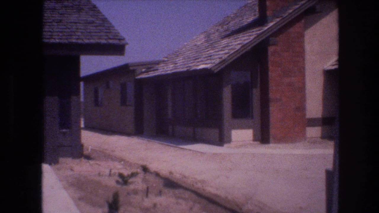 Street-level view between two low houses with dry ground and a sidewalk.