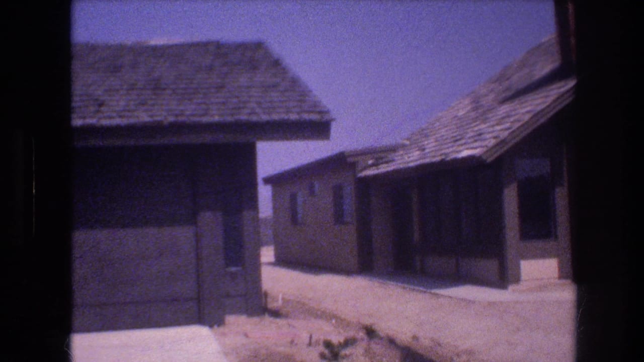 Single-story stucco houses with shingled roofs beside a dirt road.
