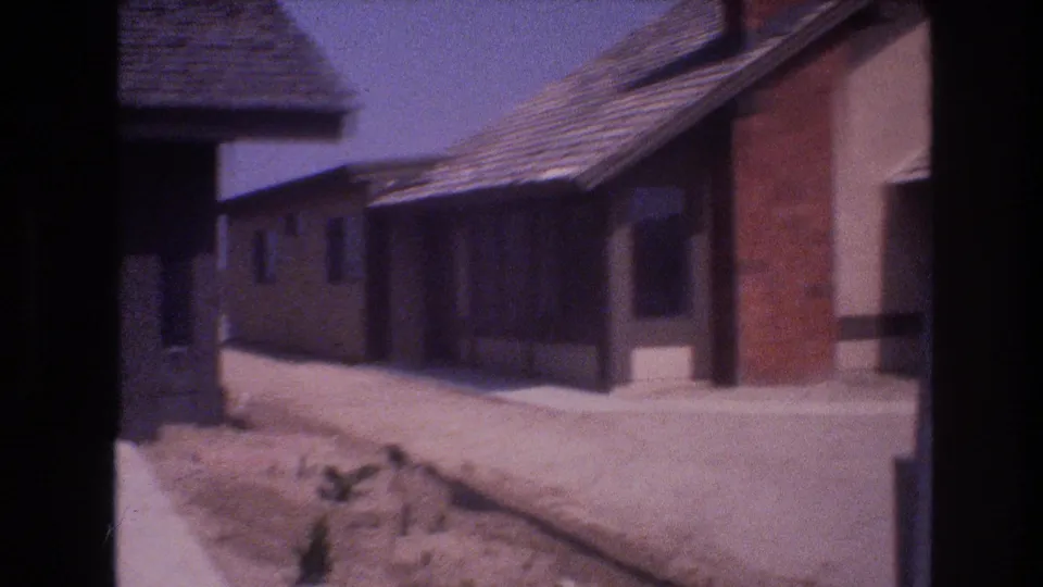 1977 Las Vegas home-movie frame with a closer view of single-story stucco homes, a dark garage bay, shingled roofs, and dry unplanted lots.