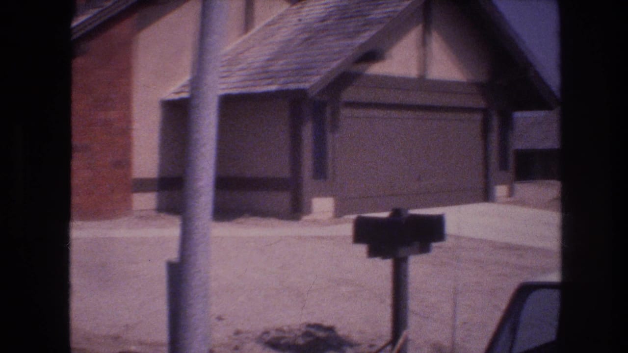 1977 Las Vegas residential exterior with an attached garage, shingled roof, utility pole, curbside mailbox, and paved street under bright light.