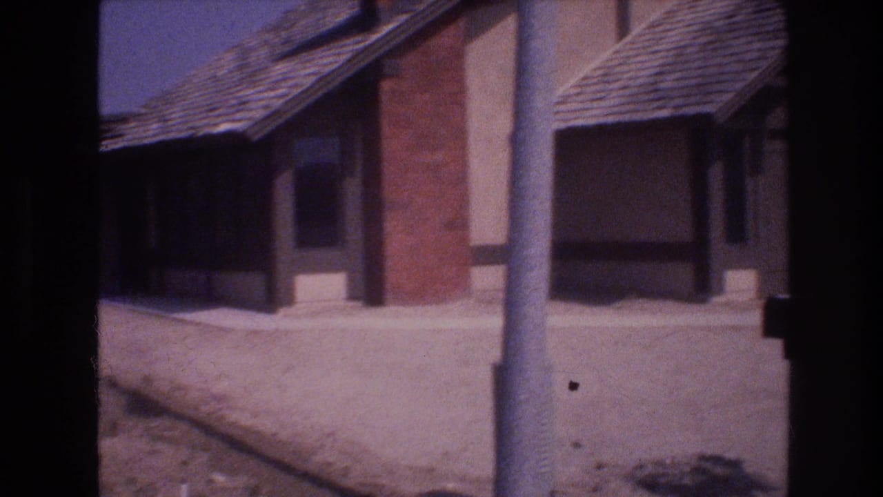 Stucco house with brick chimney, sloped roof, dry ground, and a pole in front.