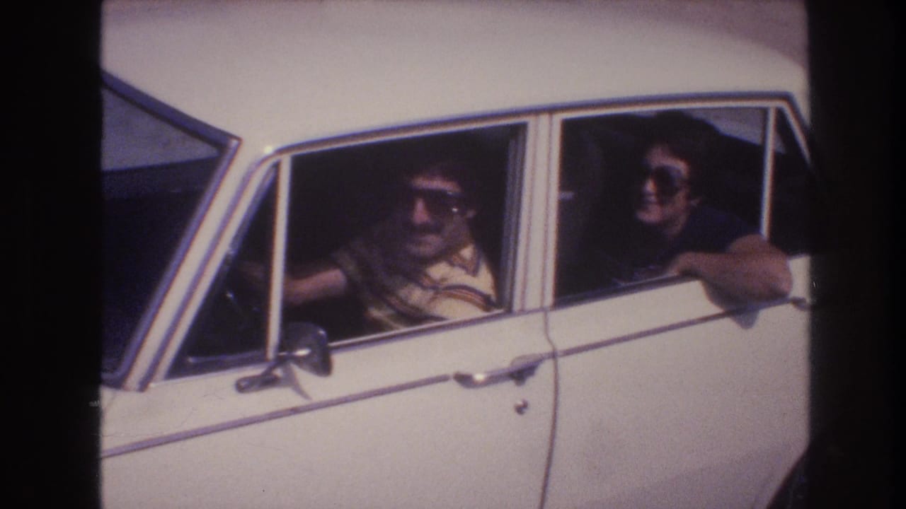 Driver and rear passenger in sunglasses look out from a white sedan.