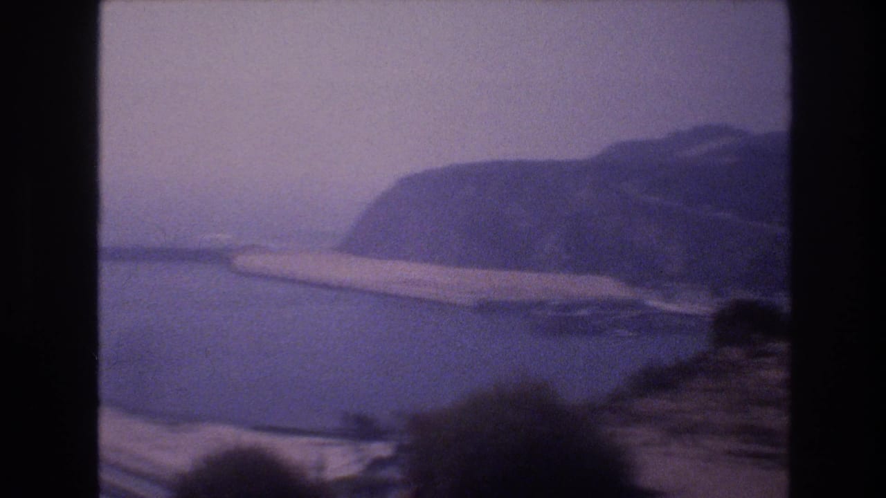 Scenic home-movie frame showing a body of water, shoreline, and hazy hills near the Las Vegas-area travel sequence.