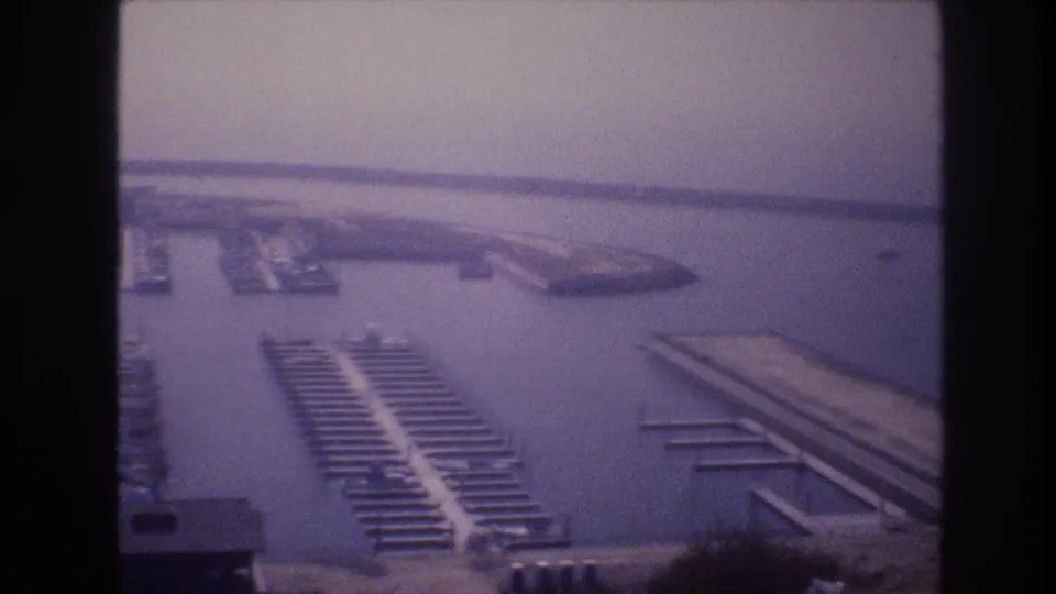 Soft 1977 8mm aerial view of a Las Vegas-area marina, showing long dock rows, small boats, shoreline, and a hazy horizon.