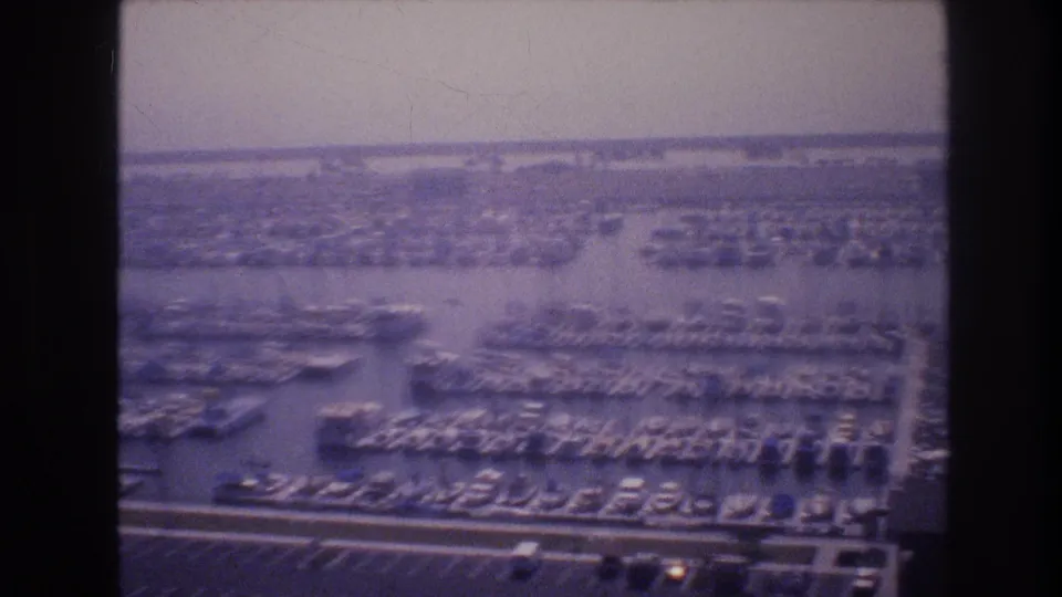 1977 8mm aerial view in Las Vegas, Nevada, showing a large marina packed with docked boats, slips, waterfront channels, and parking areas under hazy light.