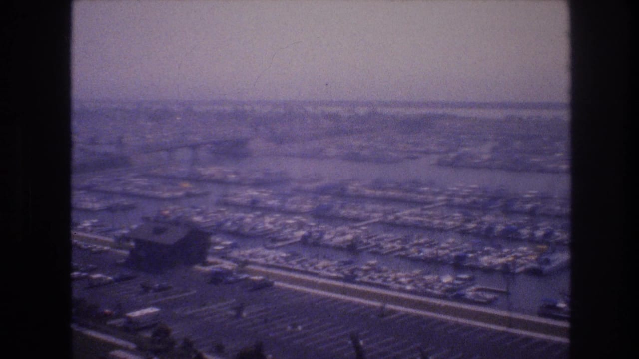 Soft purple-tinted 1977 aerial view of a Las Vegas marina, with dense boat slips, dark foreground structures, parking rows, and a hazy distant shoreline.