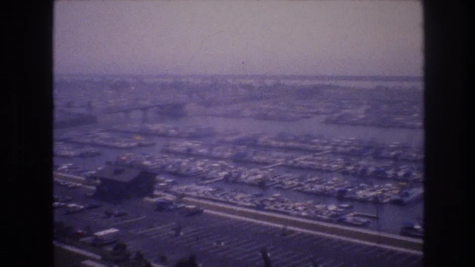 Soft purple-tinted 1977 aerial view of a Las Vegas marina, with dense boat slips, dark foreground structures, parking rows, and a hazy distant shoreline.