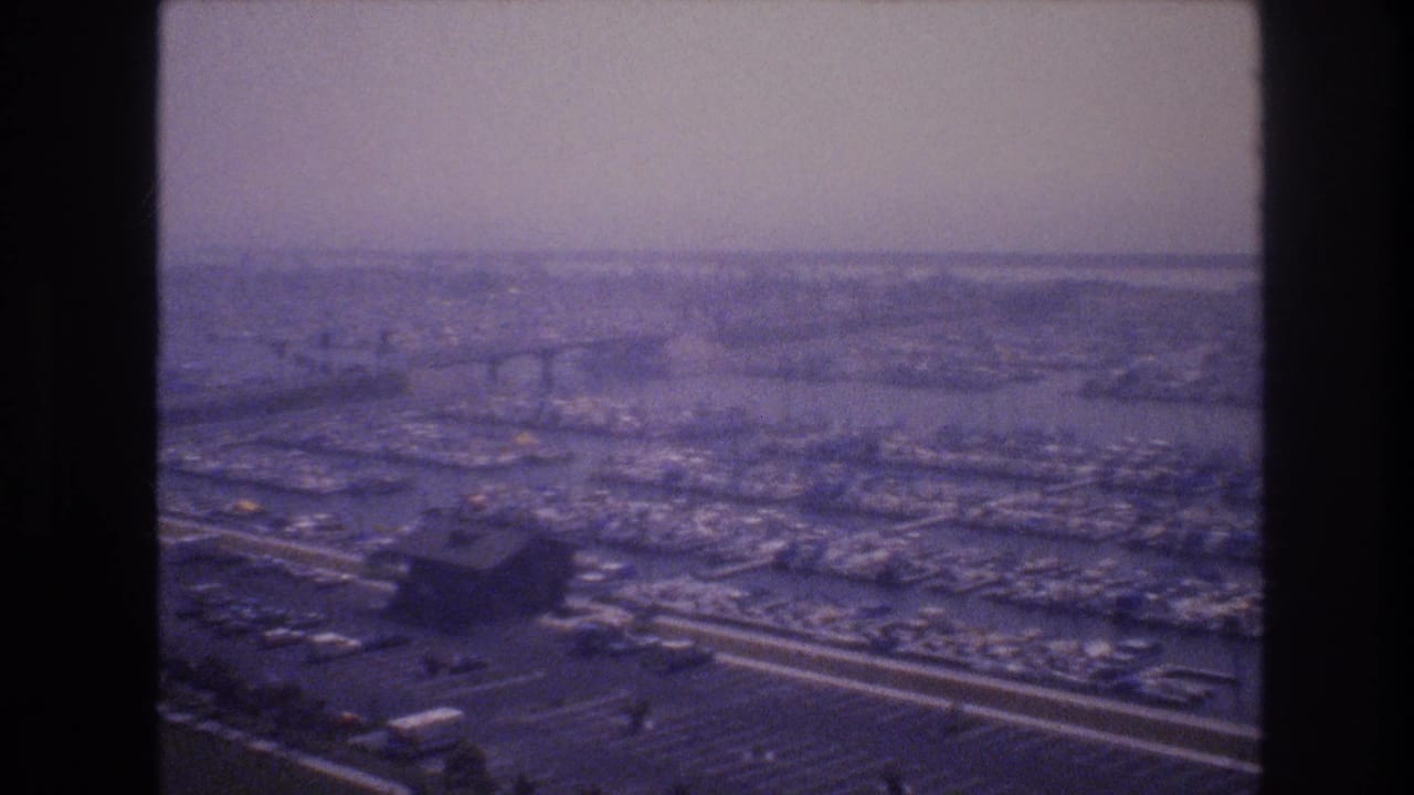 Hazy elevated view over roads, parking areas, water, and distant urban development.