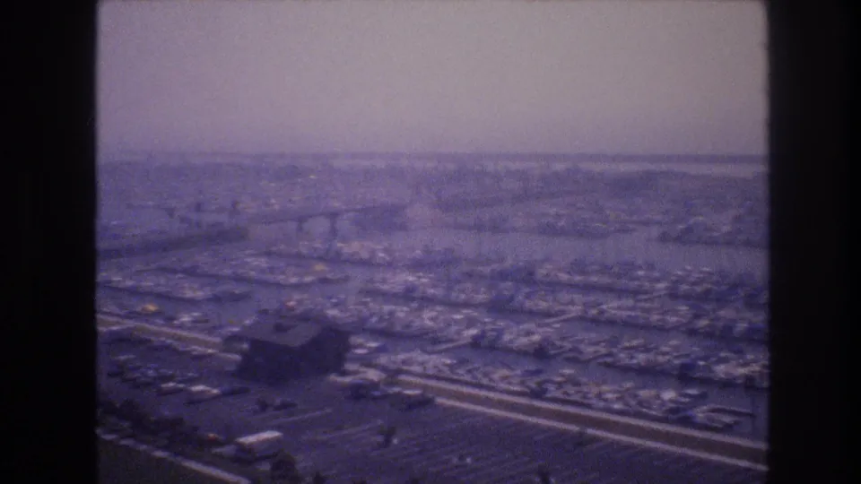 1977 8mm elevated view associated with Las Vegas, showing a hazy urban landscape with highways, parking areas, water, and distant bridge-like forms.
