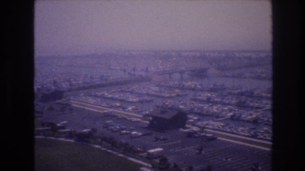 1977 8mm frame associated with Las Vegas, looking across a hazy cityscape with curving highways, waterfront structures, and dense low-rise development.