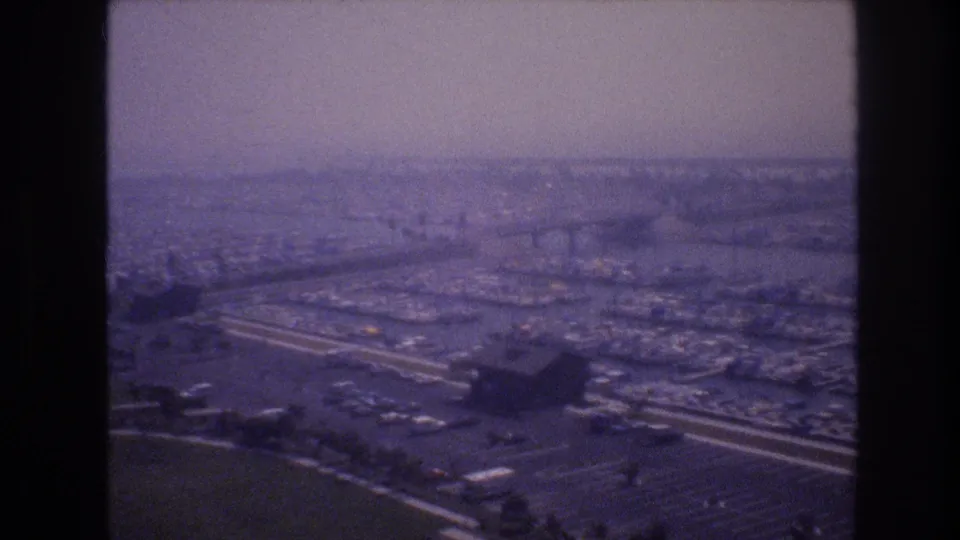 1977 8mm frame associated with Las Vegas, looking across a hazy cityscape with curving highways, waterfront structures, and dense low-rise development.