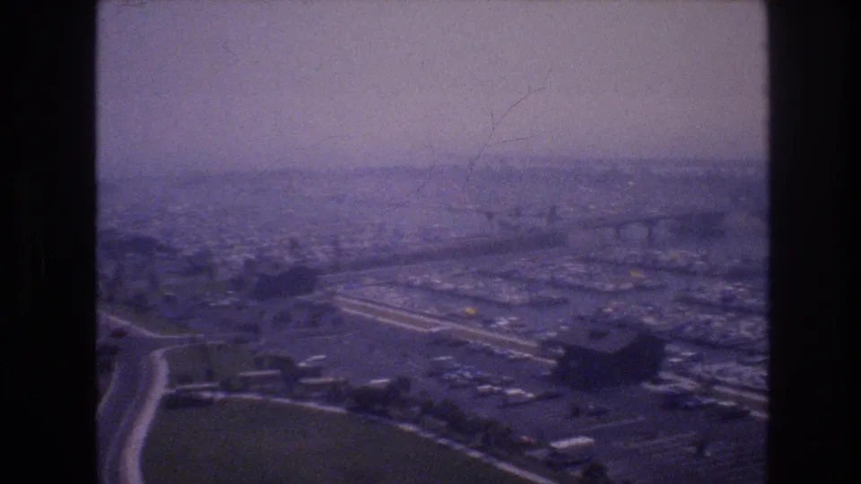 1977 8mm elevated Las Vegas-associated city view with soft focus, showing roads, parking lots, waterfront development, and distant urban haze.