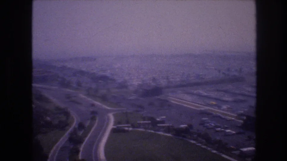 1977 8mm frame associated with Las Vegas, with a curving highway in the foreground and water, low buildings, and distant development beyond.