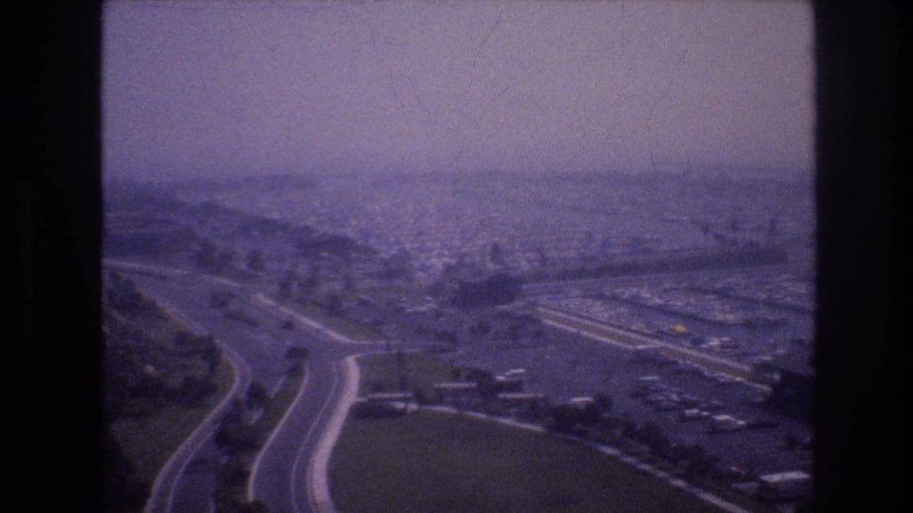 Aerial view of curving roads, parking areas, low buildings, and open land under haze.