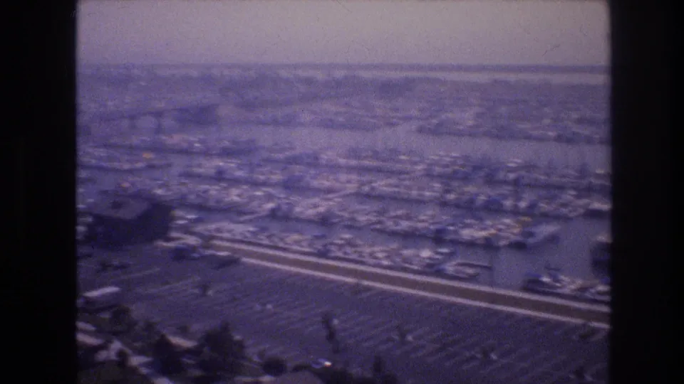 1977 Las Vegas-area 8mm aerial frame showing a highway beside a large parking lot and marina water filled with docked boats.