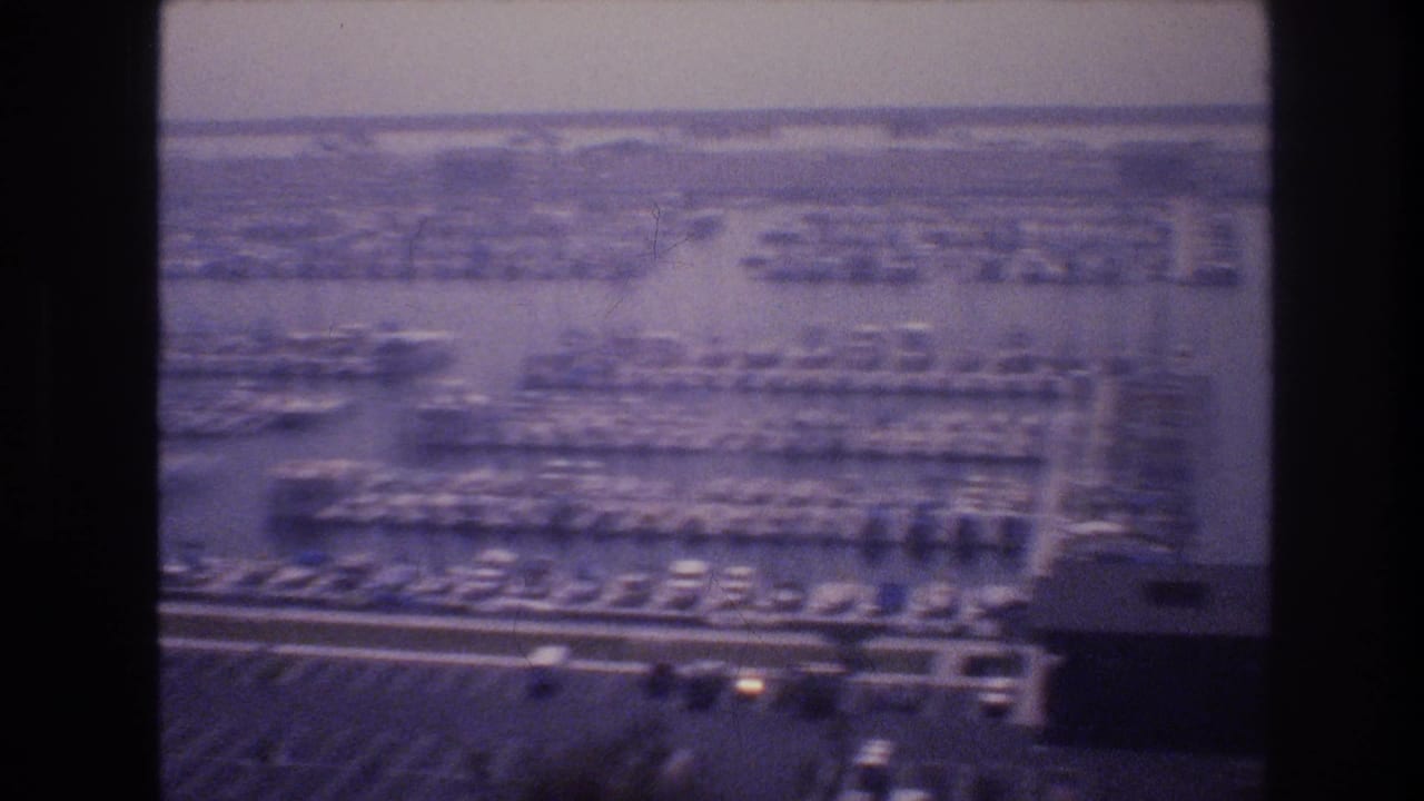Elevated view of a densely packed marina with rows of moored boats in finger slips, shot on faded 8mm film, possibly at a desert-lake marina, USA, circa 1977.
