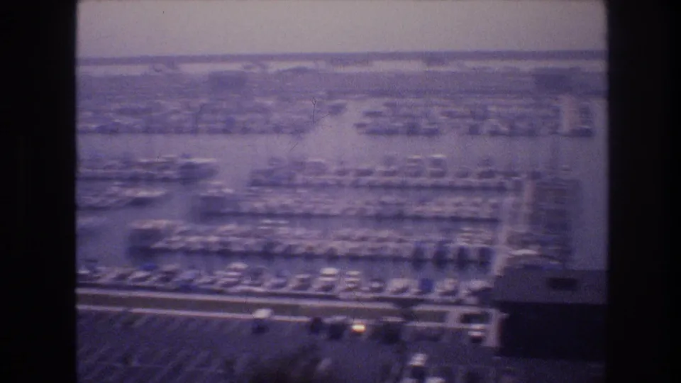 Elevated view of a densely packed marina with rows of moored boats in finger slips, shot on faded 8mm film, possibly at a desert-lake marina, USA, circa 1977.