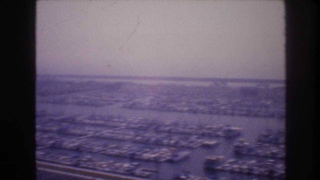 Distant urban landscape with roads, parking rows, and buildings under a hazy sky.