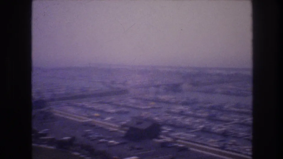 Wide 8mm frame from an elevated Las Vegas viewpoint showing roads, open ground, parking areas, and scattered buildings in soft haze.