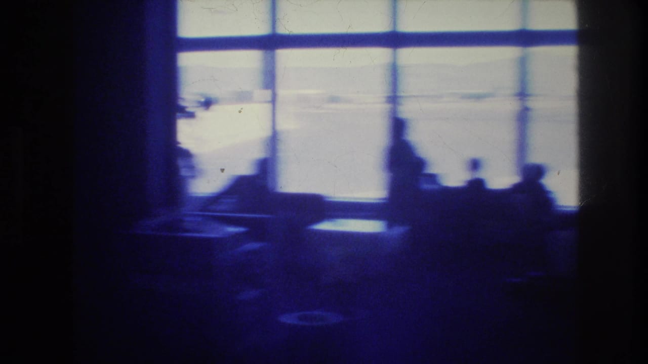 1977 Las Vegas airport terminal interior seen in silhouette, with bright windows, seating areas, and indistinct travelers in a dim blue 8mm frame.