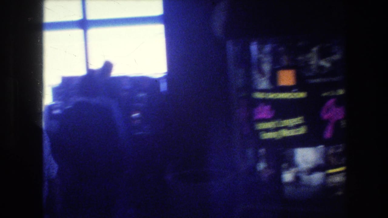 Low-light 1977 Las Vegas airport terminal view with silhouetted travelers, bright windows, and indistinct illuminated signage or display panels at right.