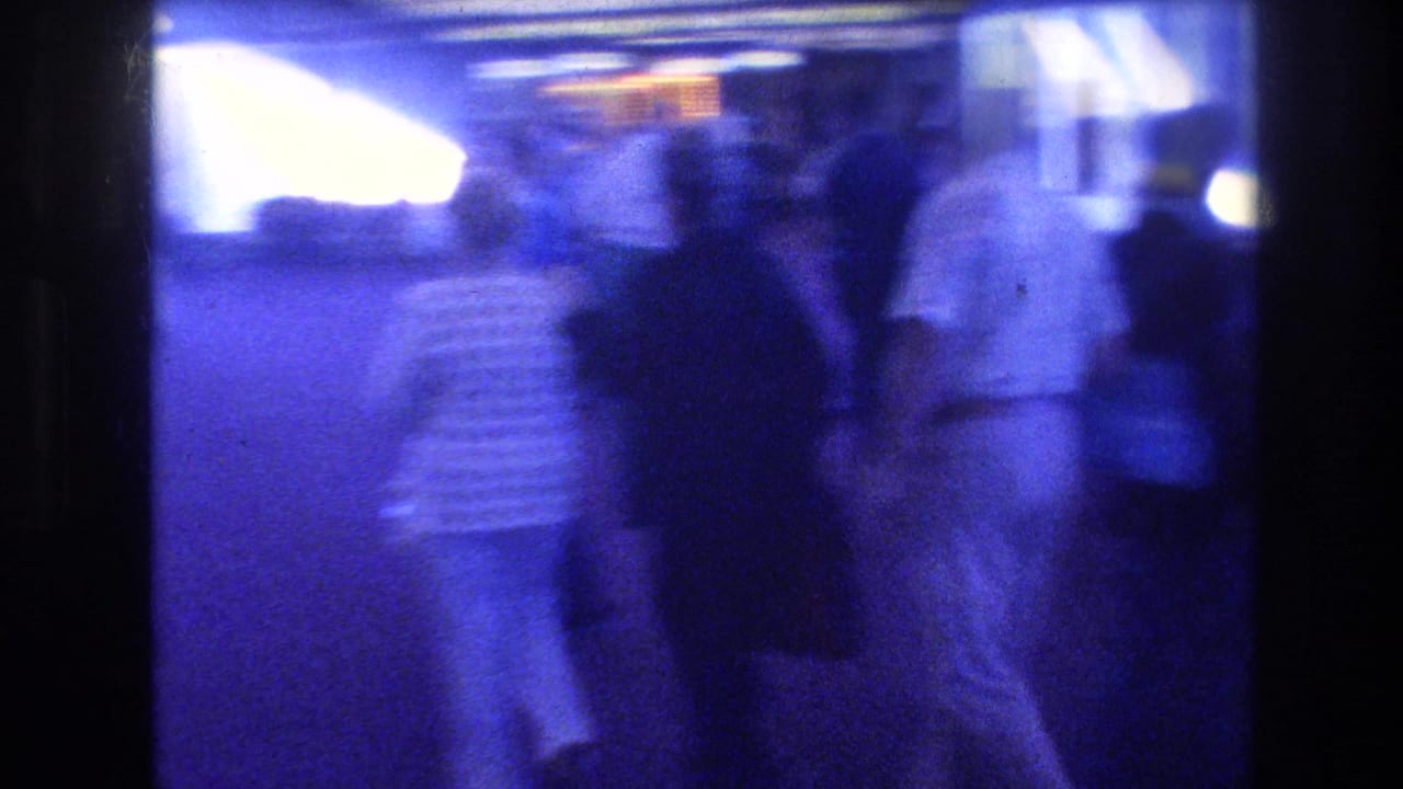 Blue-tinted, motion-blurred shot of people walking in a brightly backlit corridor or hallway.