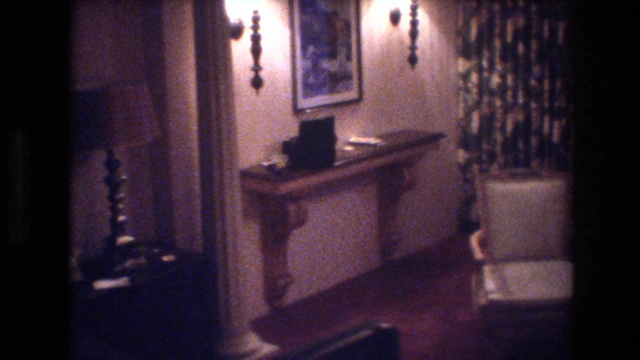 Room interior with candlestick wall sconce, carved console table, framed artwork, and patterned curtains on the right wall.