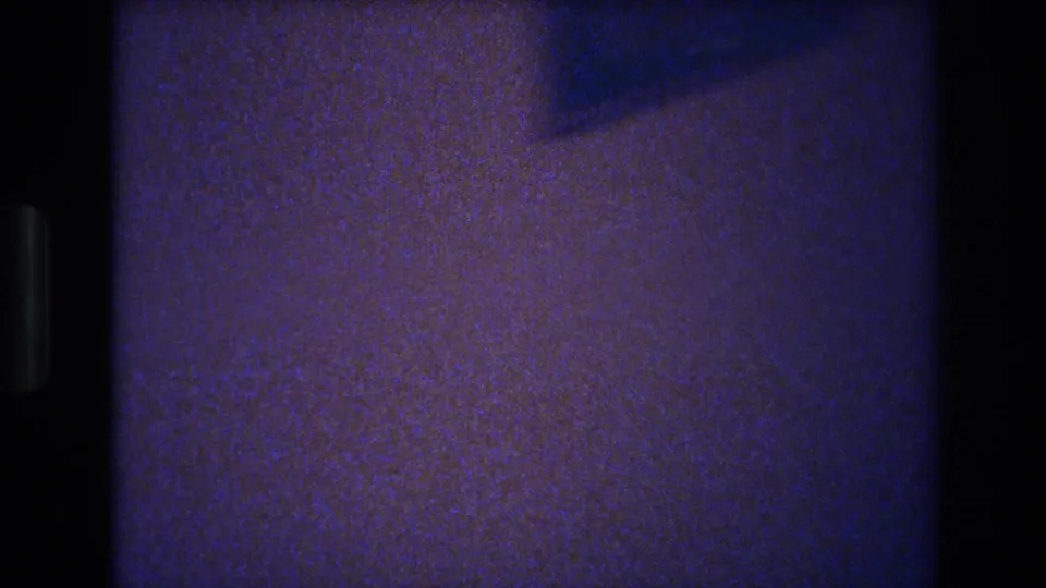 Transitional or camera-movement frame from a 1977 home movie — almost entirely dark with film sprocket edge visible.
