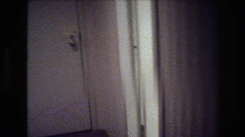 Interior doorway or window area in a 1977 Las Vegas home showing white walls, vertical light streaks, and 8mm film grain.