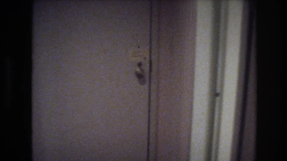 Hotel or motel room door with small latch, cream-painted interior walls — establishing shot consistent with 1970s American travel accommodation.