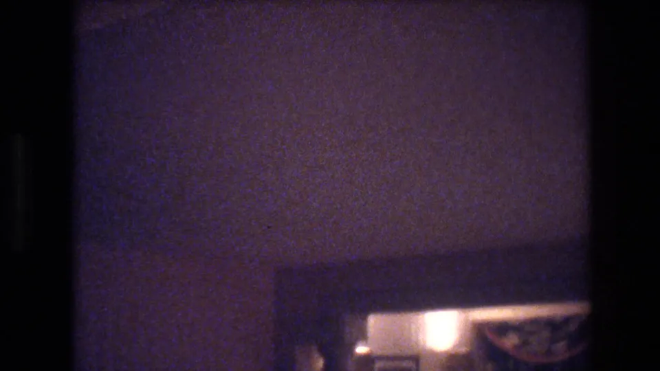 Heavily underexposed 8mm hotel room interior, Las Vegas, circa 1977, showing a warm lamp and dark curtain before the camera turns toward the window.