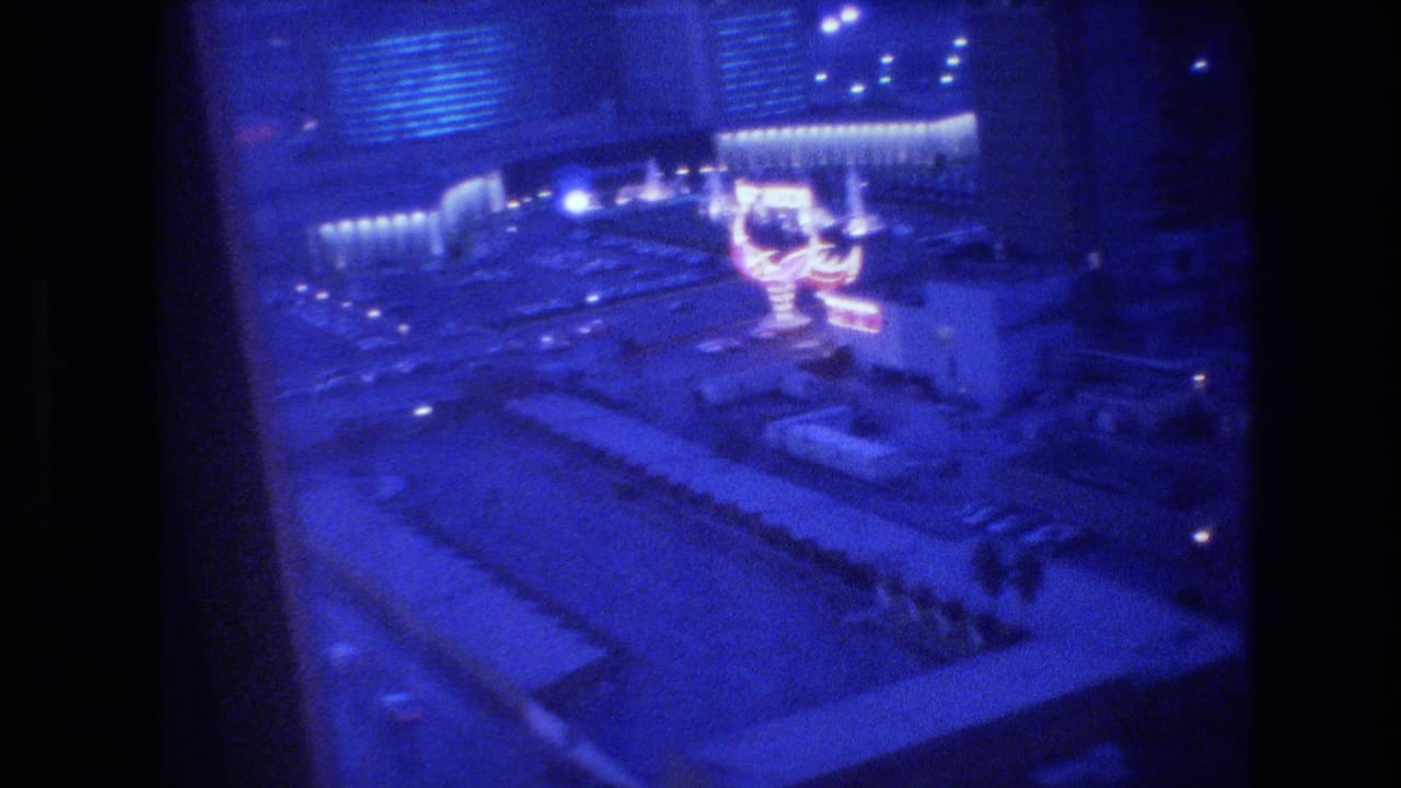 Elevated night view of Las Vegas showing a large neon sign and hotel buildings with a deep blue 8mm color cast.