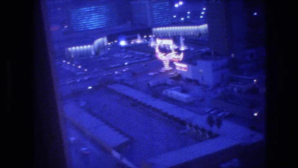 Tourist's elevated 8mm view of Las Vegas at night, circa 1977, with a large neon cocktail-glass sign glowing in orange-pink below.