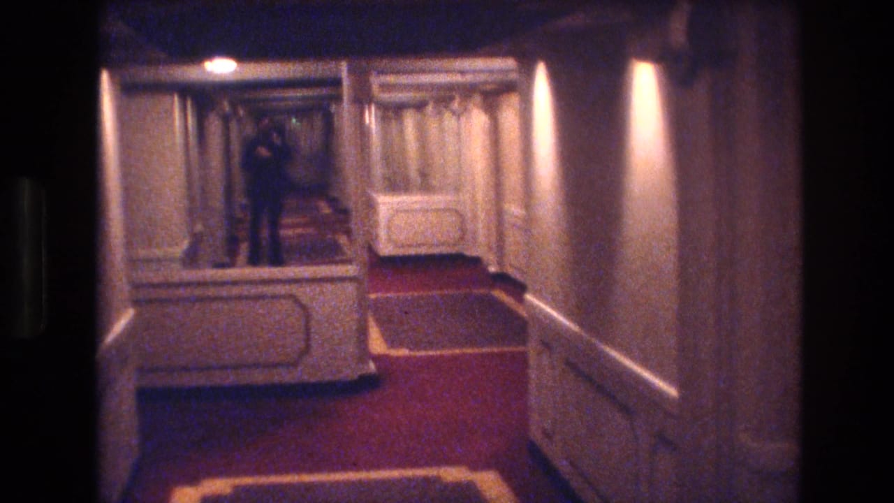 1977 Las Vegas hotel corridor view with red carpeting, cream paneled walls, warm lights, curtains, and a distant person standing near the far end.