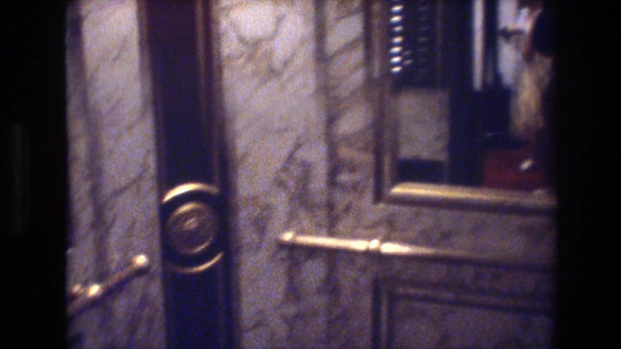 8mm shot of ornate elevator doors with gold trim and brass call button on a marble wall in a 1977 Las Vegas casino hotel.