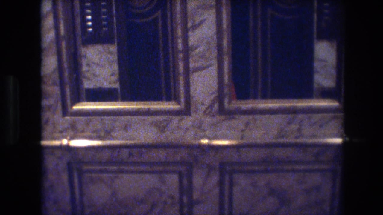 8mm frame of closed gold-framed elevator doors set in marble, with a floor button panel visible, in a 1970s Las Vegas casino hotel.
