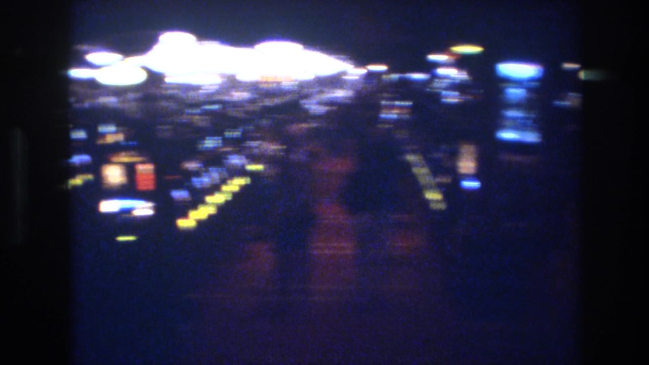 8mm low-light shot of a Las Vegas casino floor with multicolored glowing slot machines receding into darkness, circa 1977.