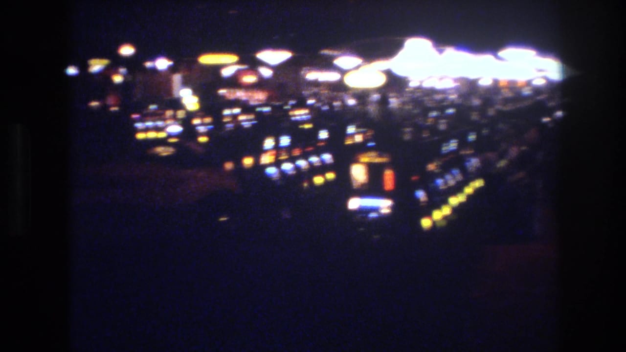Dark casino interior with rows of illuminated slot machines, yellow coin-tray lights, and blue machine displays receding into shadow.