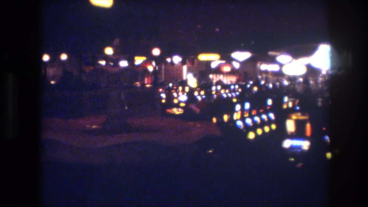 Casino floor with slot machine banks extending into darkness, yellow indicator lights in rows, and scattered overhead circular lighting visible.