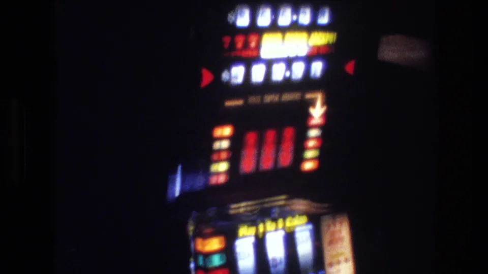 Final frame of 1977 Las Vegas slot machine showing 'Play 1 to 5 Coins' coin panel, colored jackpot pay table, red arrows, and reel window — 8mm film grain throughout.