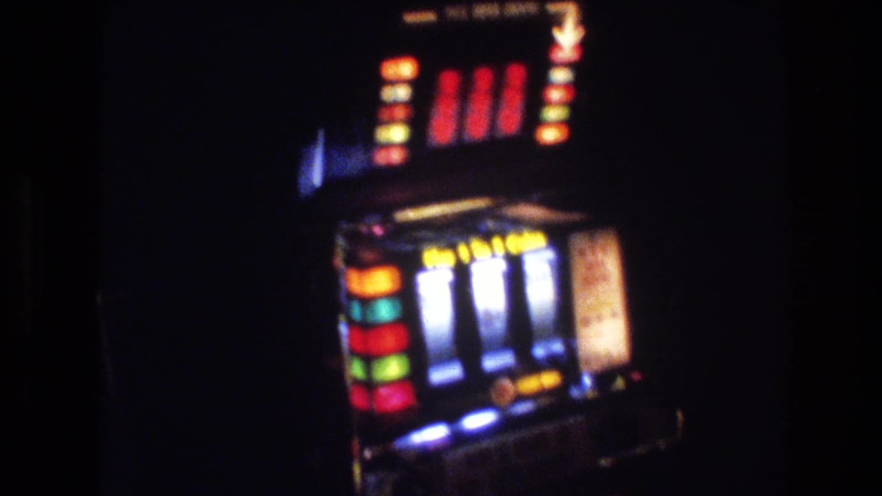 Close-up of a mechanical slot machine with multi-colored illuminated reel segments against a dark casino interior.