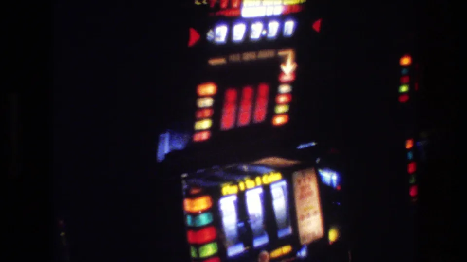 8mm close-up of a 1970s slot machine showing a jackpot or credit dollar display with arrow indicators in a dimly lit Las Vegas casino interior, circa 1977.