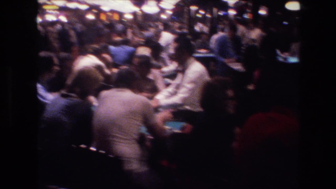 Crowded casino gaming floor with players around green-felt tables in 1970s attire, dim overhead lighting.